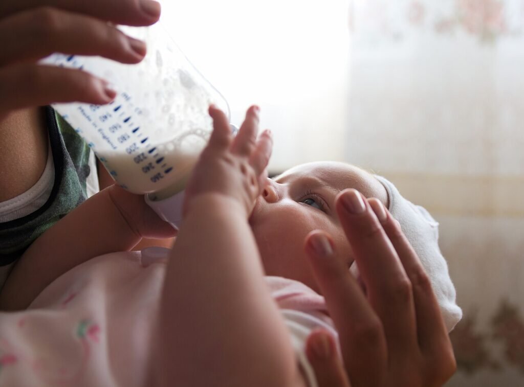 Bebé tomando biberón con acompañamiento adulto y enfoque en alimentación segura
