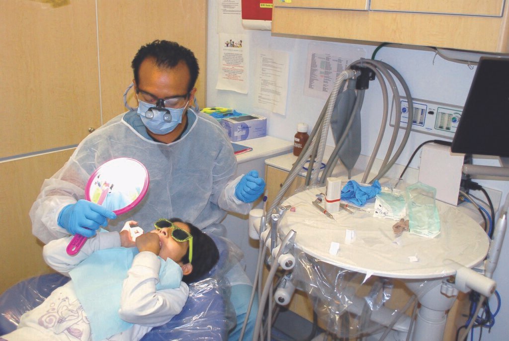 Clínica de odontopediatría con niño en sillón dental y profesional realizando tratamiento infantil